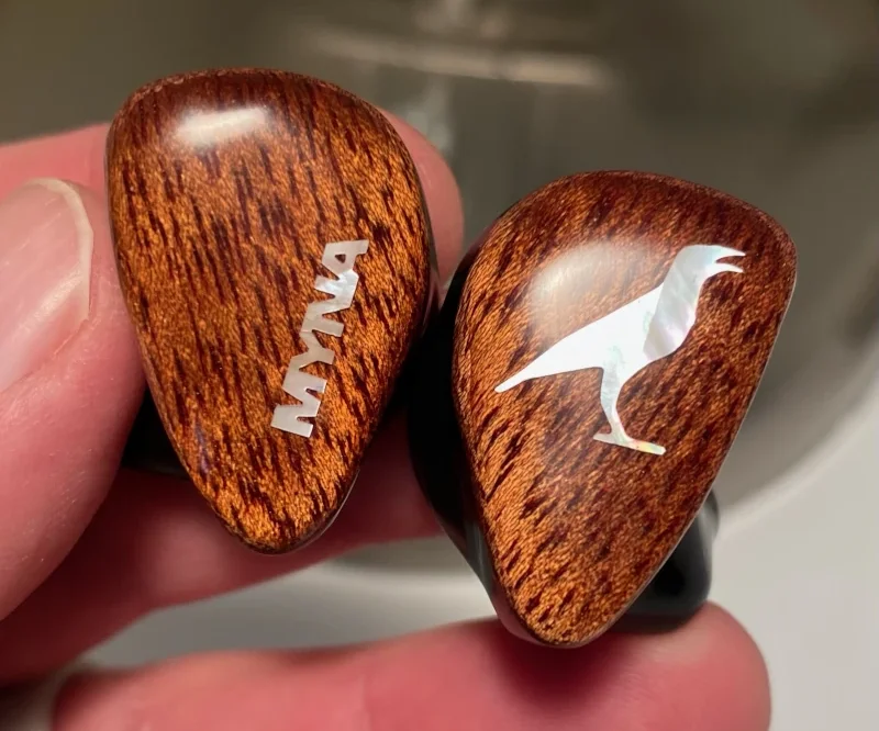 A pair of Myna custom-molded IEMs with polished bloodwood faceplates and mother-of-pearl inlays, held in hand